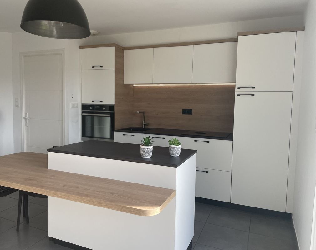 Cuisine après rénovation : îlot blanc, plan de travail et crédence en bois