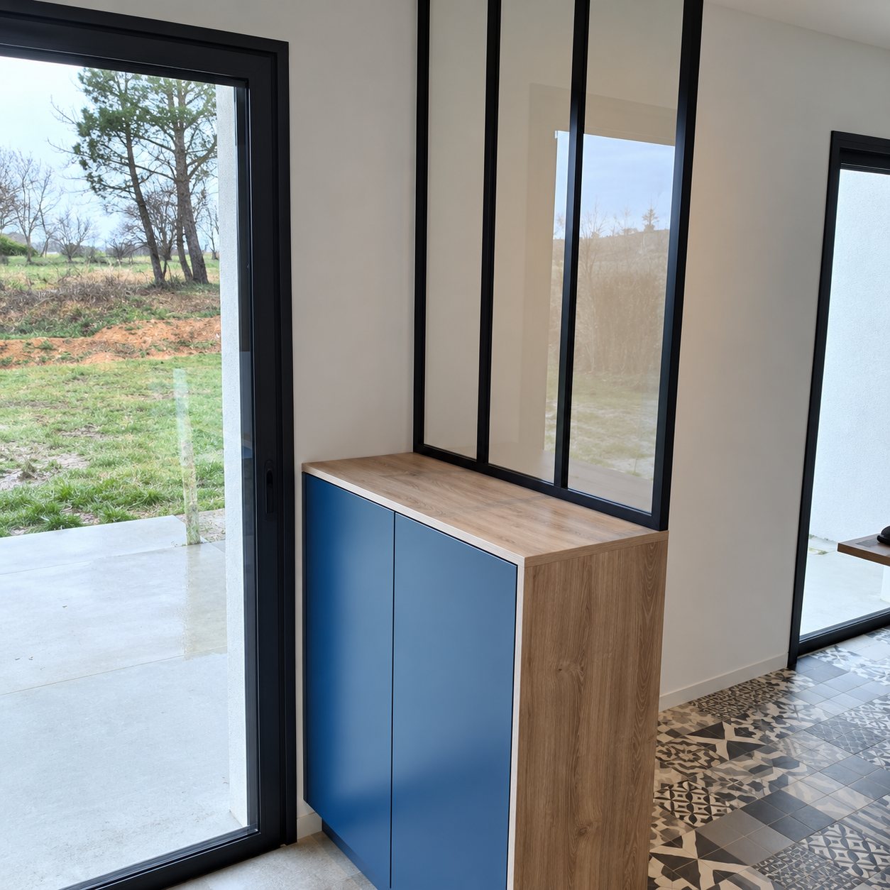 Verrière noire au-dessus d’un meuble bleu et bois dans une entrée